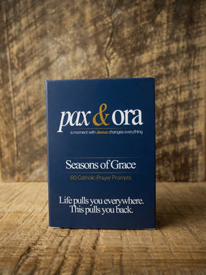 Catholic Prayer Cards — Pax & Ora Seasons of Grace deck in a navy blue box with gold text on a rustic wood background.